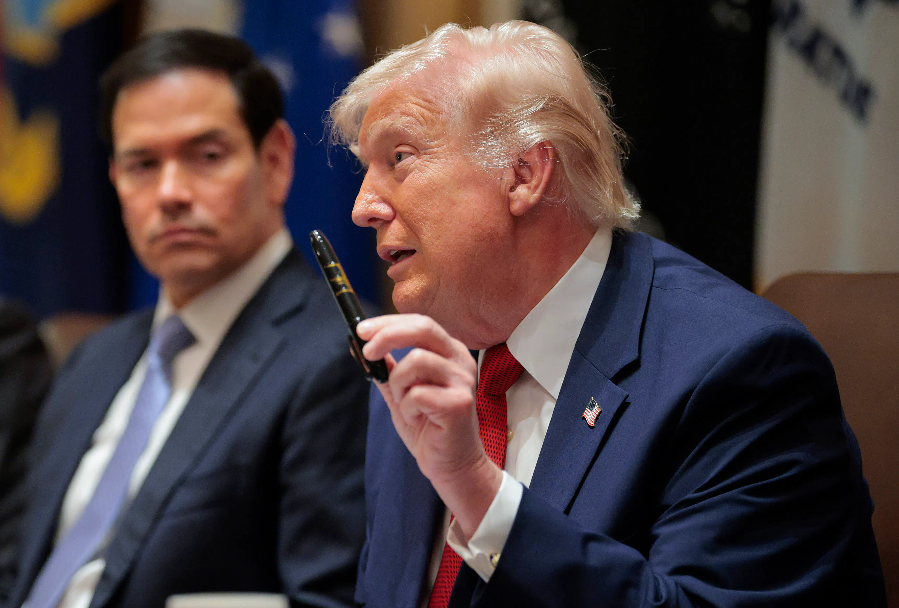 President Donald Trump holds up a Sharpie as he speaks. Secretary of State Marco Rubio, sitting next to him, looks on.