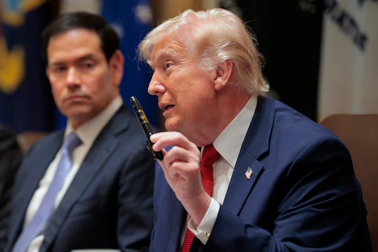President Donald Trump holds up a Sharpie as he speaks. Secretary of State Marco Rubio, sitting next to him, looks on.