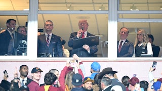 Donald Trump reads off a piece of paper into a microphone at the Commanders NFL game.