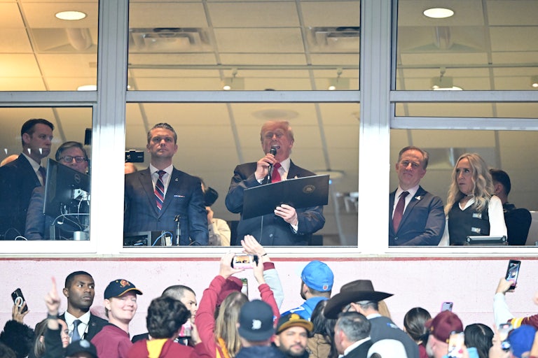 Donald Trump reads off a piece of paper into a microphone at the Commanders NFL game.