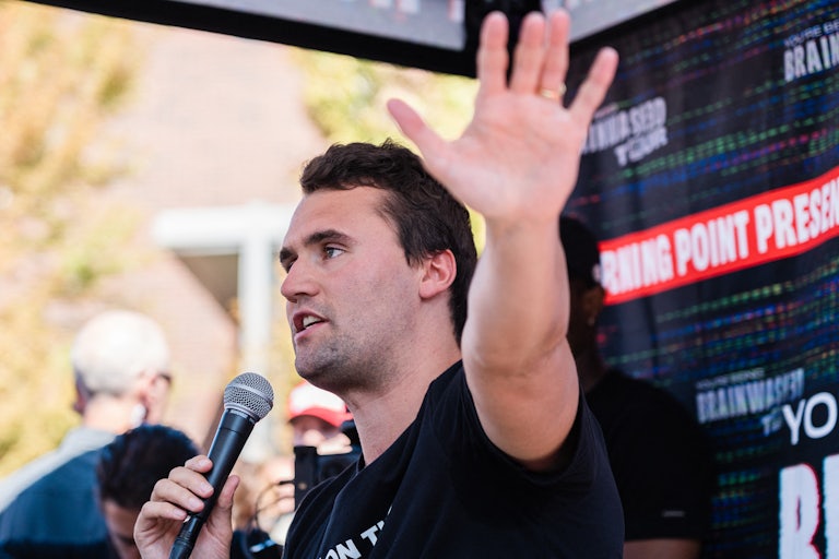 Charlie Kirk raises a hand while speaking into a microphone