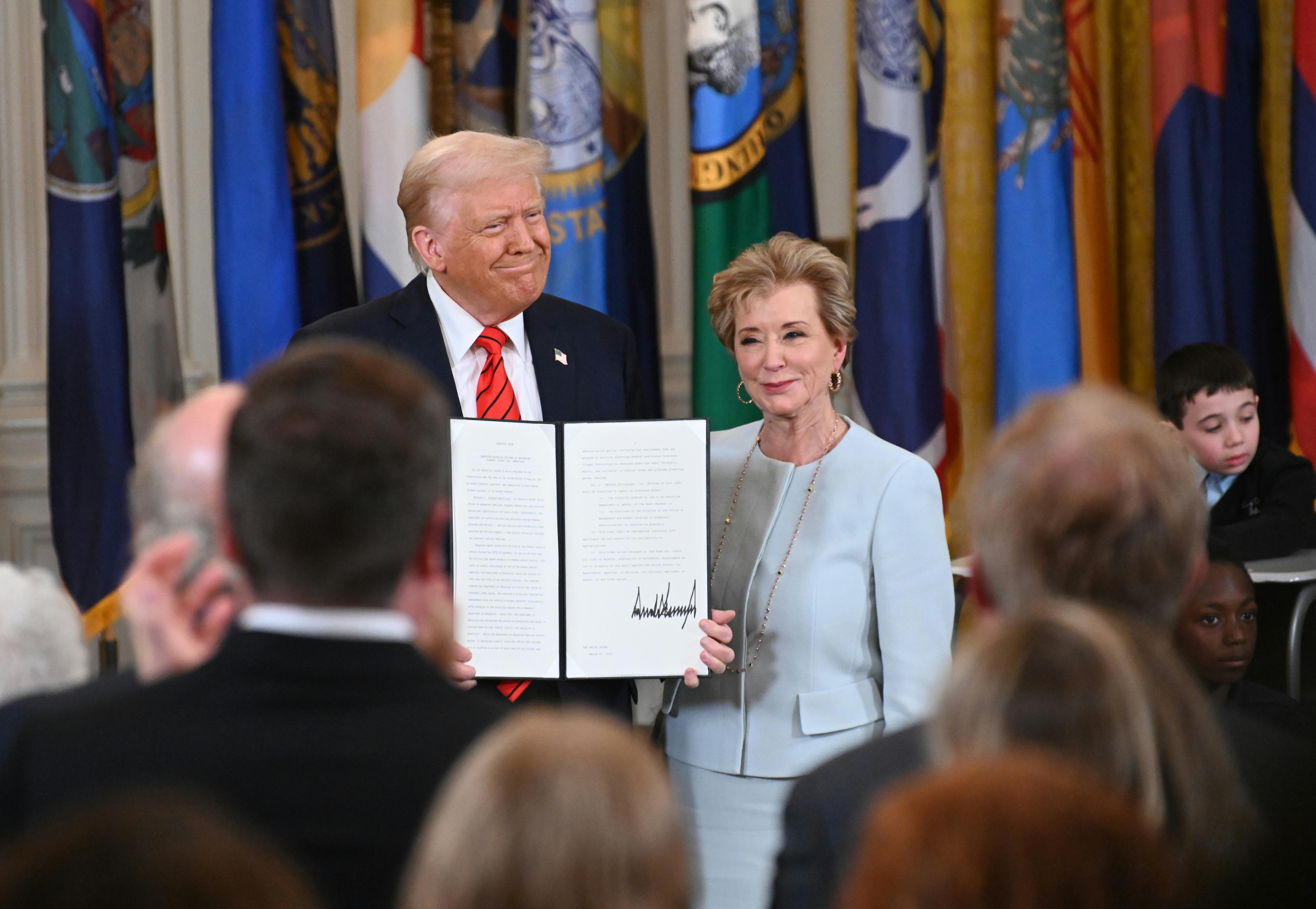 Donald Trump holds a signed executive order as he poses alongside Education Secretary Linda McMahon.