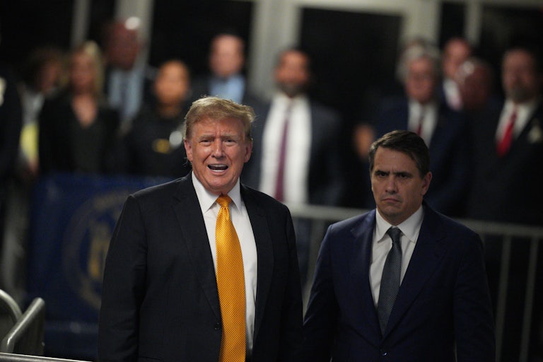 Donald Trump speaks with his mouth wide open. Todd Blanche stands beside him. Others are in the background out of focus.