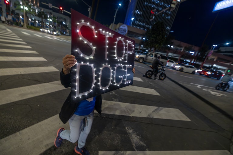 A person holds up a sign that says, "STOP DOGE" during a protest against Donald Trump and Elon Musk