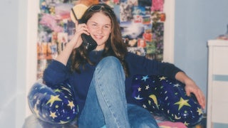 Teen wearing Y2K fashion, 2000s style, inside teenage bedroom, talking on cordless telephone, sitting on an inflatable chair, wearing flared denim jeans.