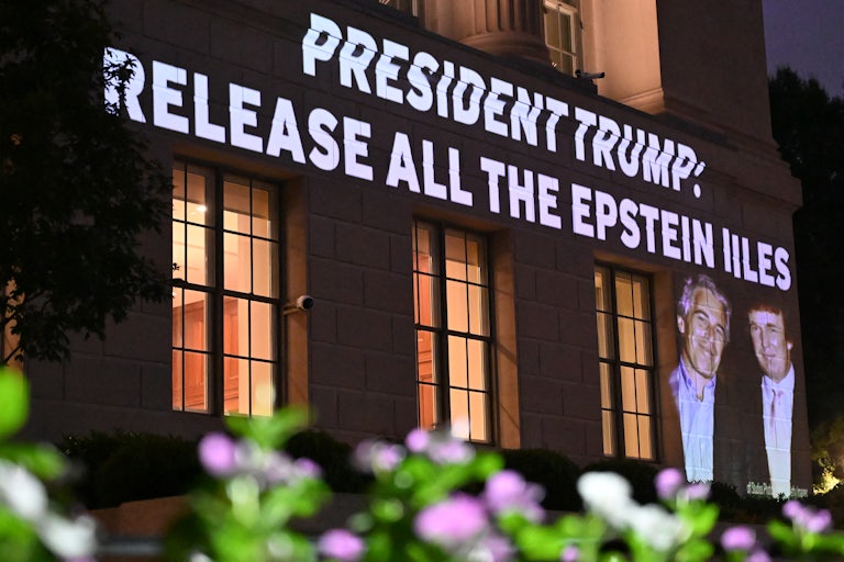 The words "President Trump: release all the Epstein Files" and a photo of Donald Trump and Jeffrey Epstein are projected onto a building