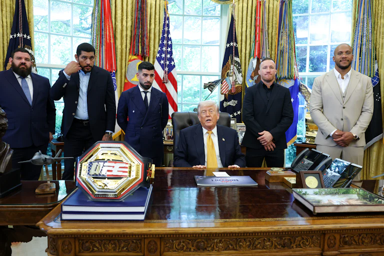 Donald Trump speaks while sitting at his desk in the Oval Office. He is flanked by four UFC fighters.