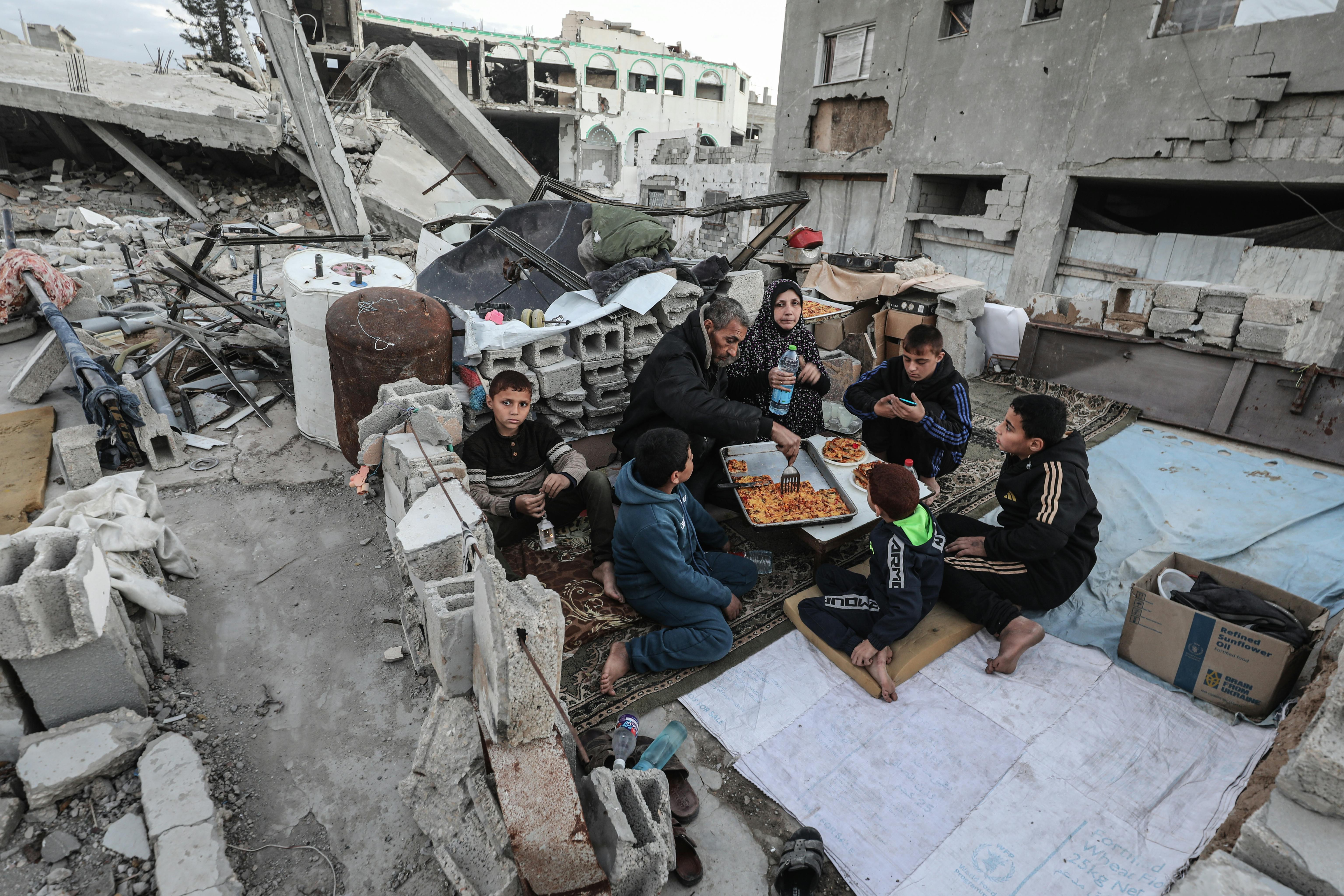 A Palestinian family with a man, woman, and five children sits amidst rubble to break their Ramadan fast