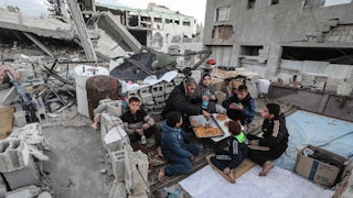 A Palestinian family with a man, woman, and five children sits amidst rubble to break their Ramadan fast
