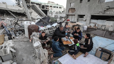 A Palestinian family with a man, woman, and five children sits amidst rubble to break their Ramadan fast