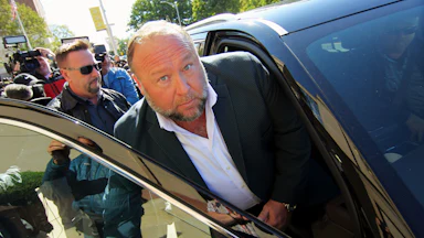 Alex Jones looks up while getting in the front passenger seat of a car