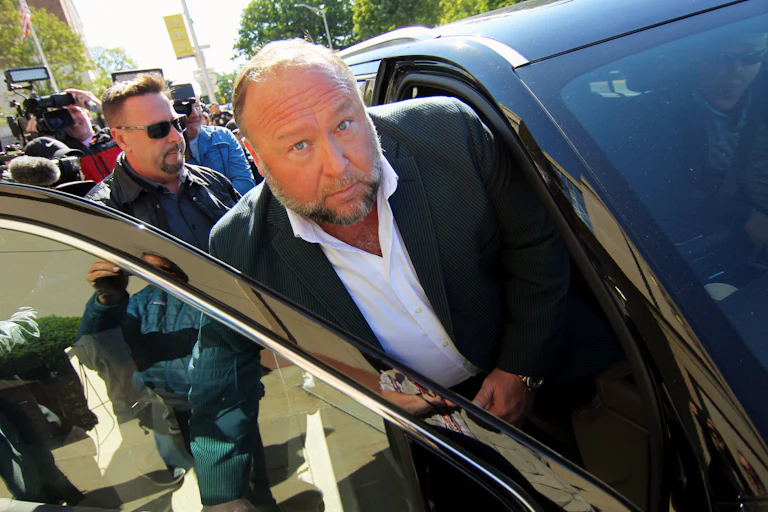 Alex Jones looks up while getting in the front passenger seat of a car