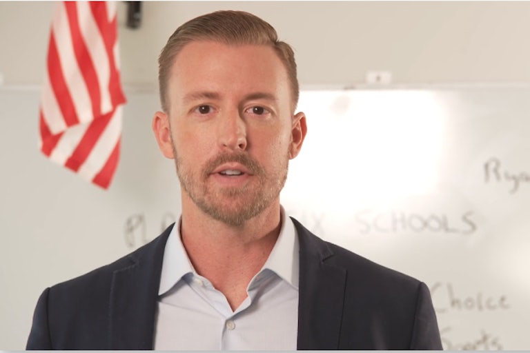 Ryan Walters speaks to the camera. A white board and an American flag are behind him.