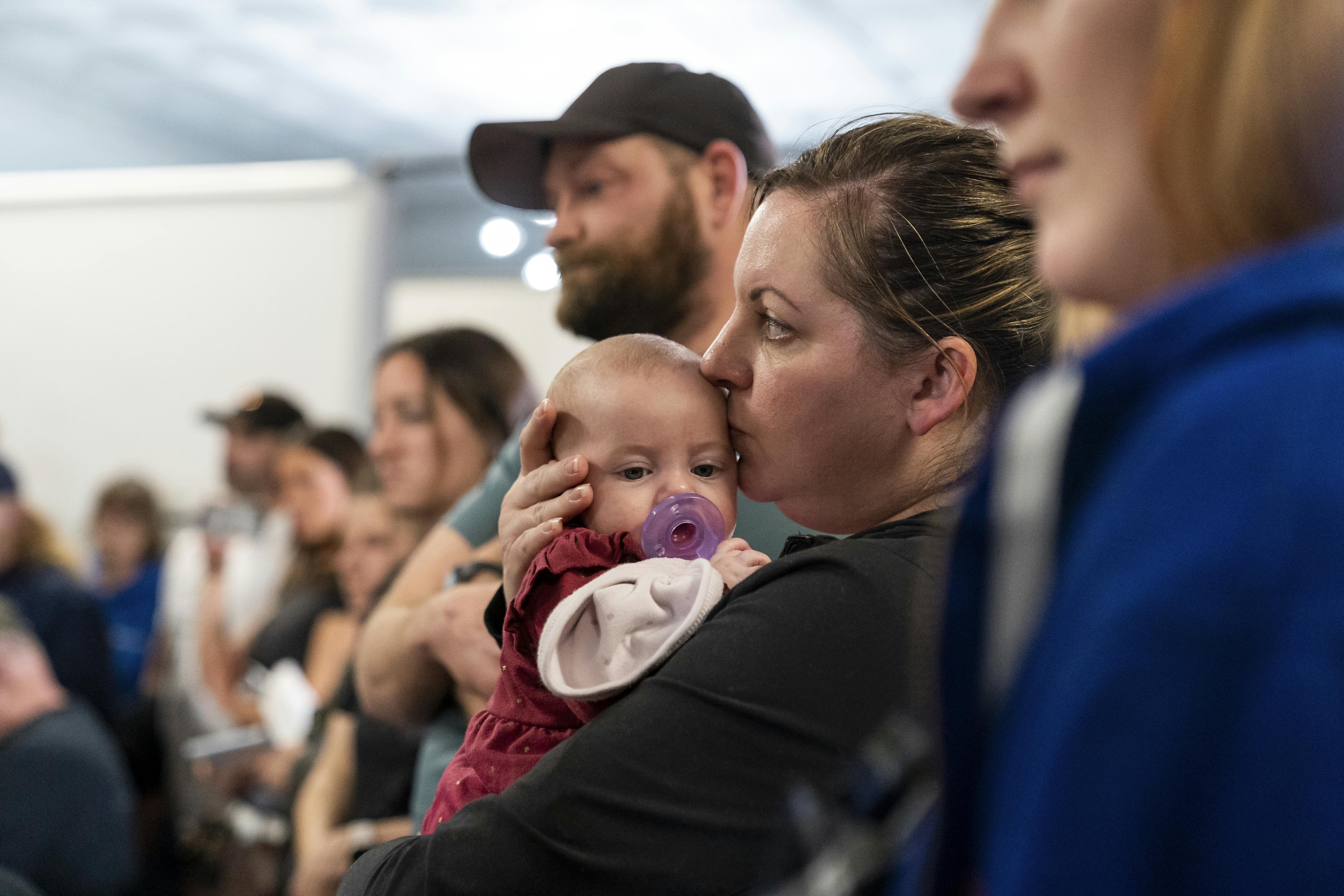 A woman stands among other people, holding a baby.