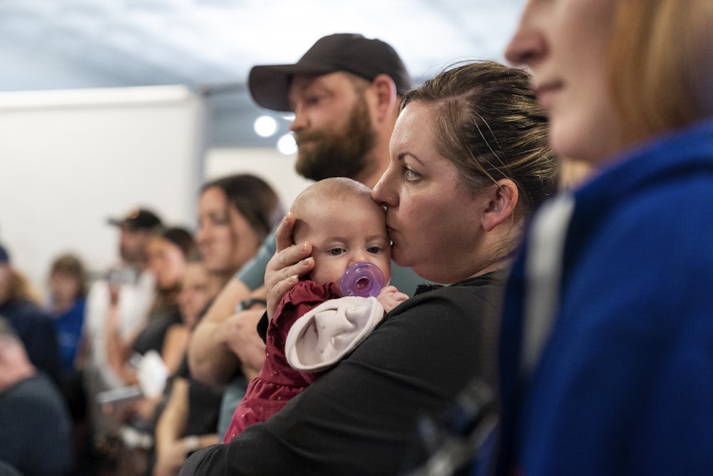 A woman stands among other people, holding a baby.