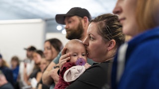 A woman stands among other people, holding a baby.