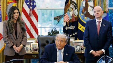 Homeland Security Secretary Kristi Noem and FIFA President Gianni Infantino stand on either side of Donald Trump, who is seated at his desk in the Oval Office of the White House.