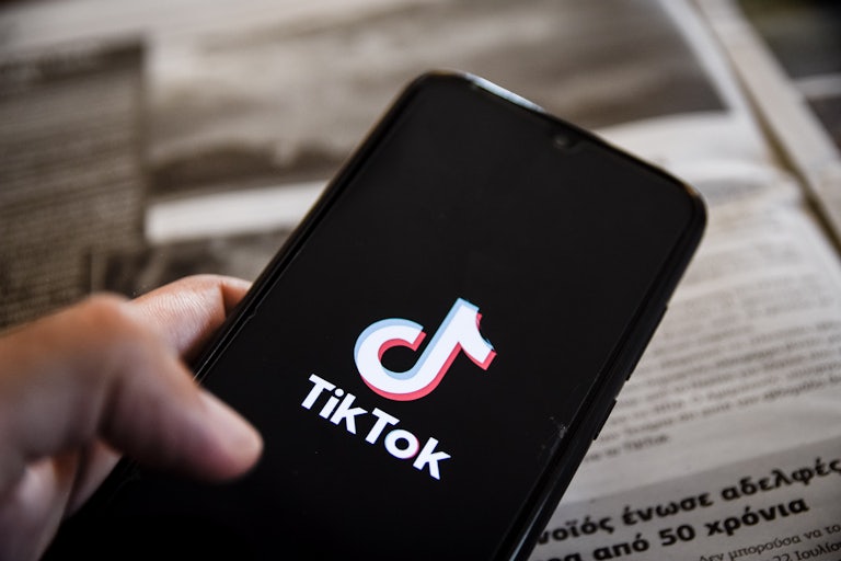 A hand holds a phone with the TikTok app loading