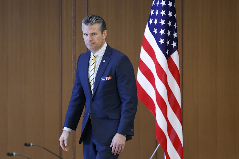 Defense Secretary Pete Hegseth stands in front of an American flag