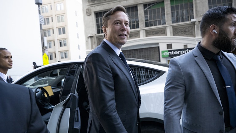 Elon Musk stands near a Tesla outside