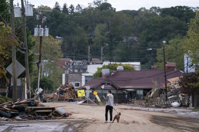 A woman and her dog walk amid crumbled buildings in the aftermath of Hurricane Helene