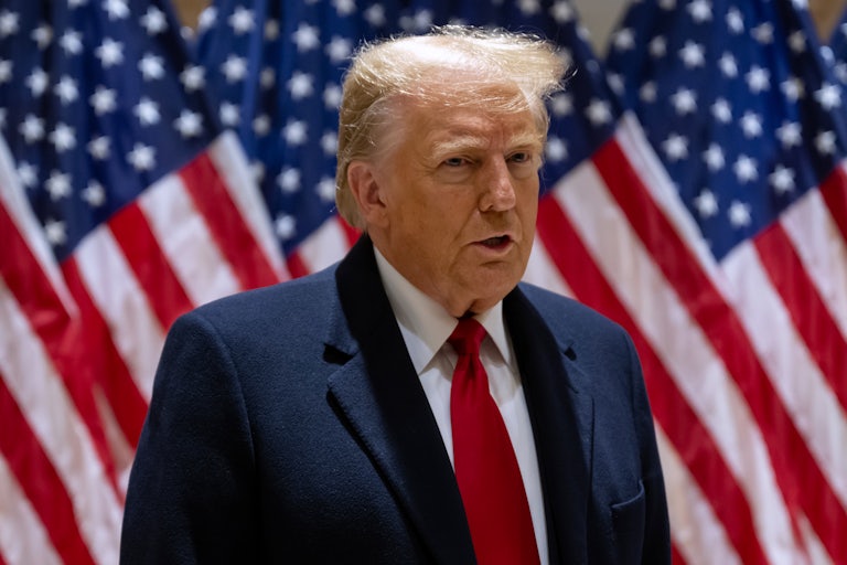 Donald Trump speaks and looks off camera. A row of U.S. flags are behind him.