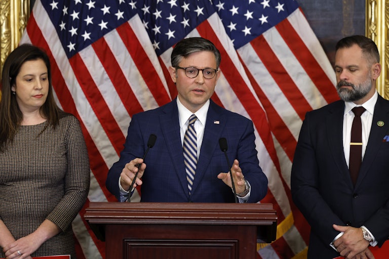 House Speaker Mike Johnson speaks at a podium. Representatives Elise Stefanik and Cory Mills stand on either side of him.