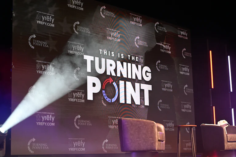 The Turning Point USA logo is projected onto an onstage screen