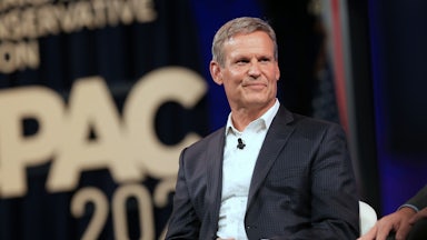 Tennessee Governor Bill Lee is seated on stage and smiles. The words CPAC appear behind him.