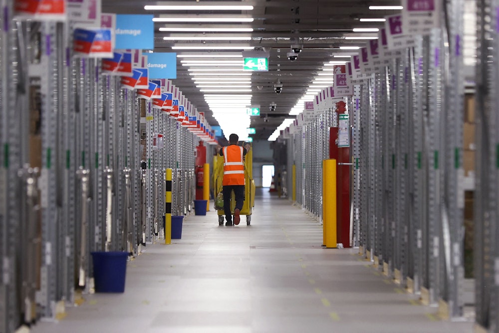 A worker in an orange safety vest pushes a cart of packages at an Amazon warehouse.