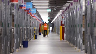 A worker in an orange safety vest pushes a cart of packages at an Amazon warehouse.
