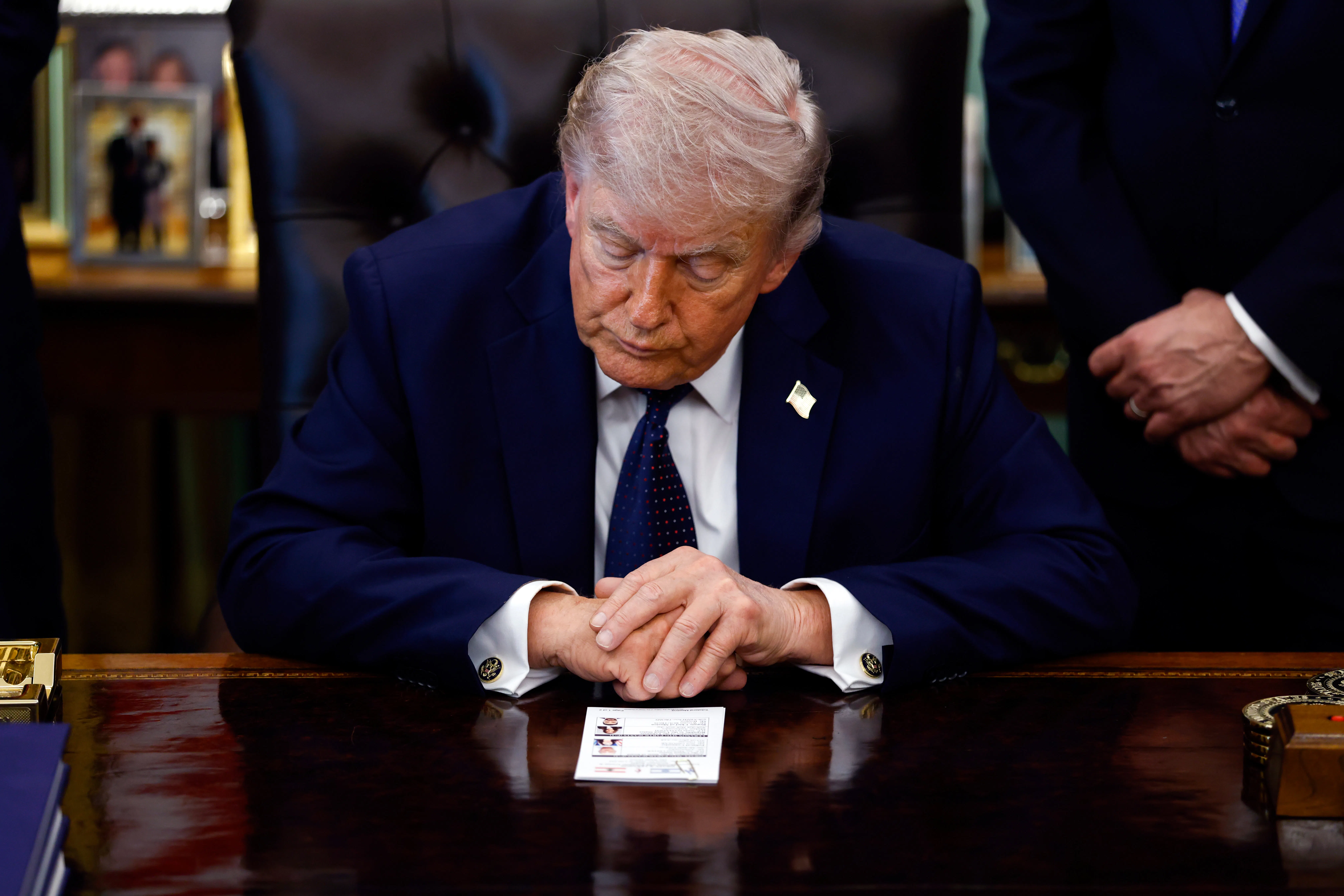 Donald Trump leans forward on his desk in the Oval Office with his eyes closed