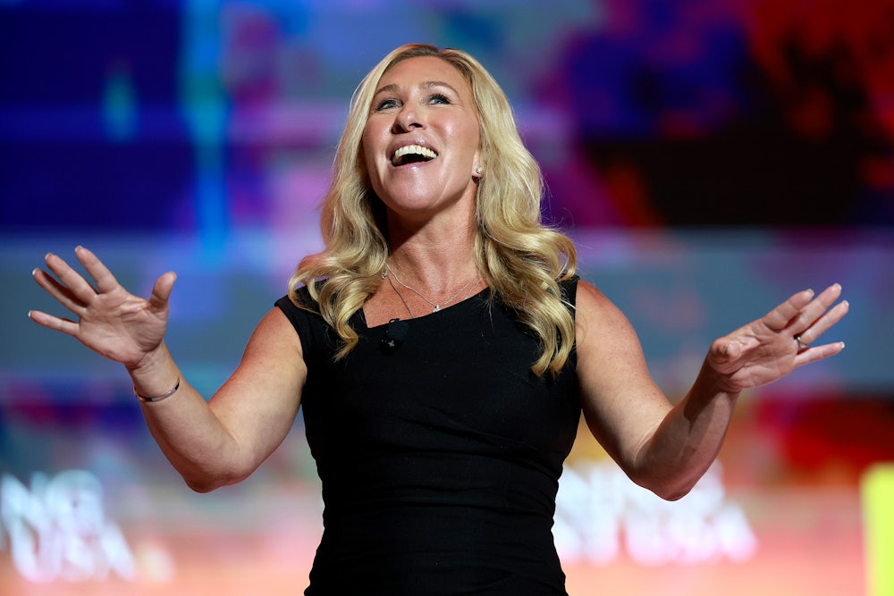 Marjorie Taylor Greene holds her arms out while smiling.