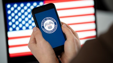Someone holds a phone with the SSA logo in front of a U.S. flag on another screen.