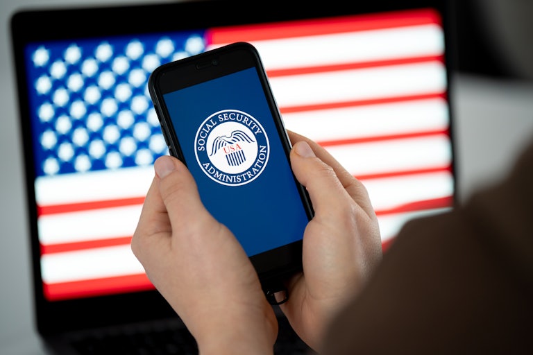 Someone holds a phone with the SSA logo in front of a U.S. flag on another screen.