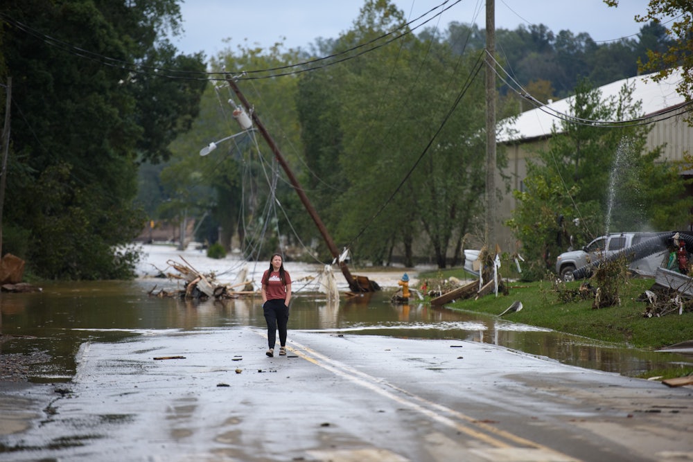 A woman stands on a flooded street in front of downed power lines.