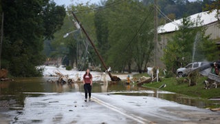 A woman stands on a flooded street in front of downed power lines.