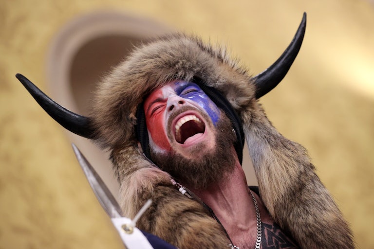 A man wearing a bull horn headdress and red, white, and blue facepaint cackles after breaking into the United States Capitol.