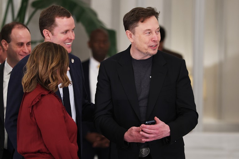 Elon Musk smiles while standing in a group of people.