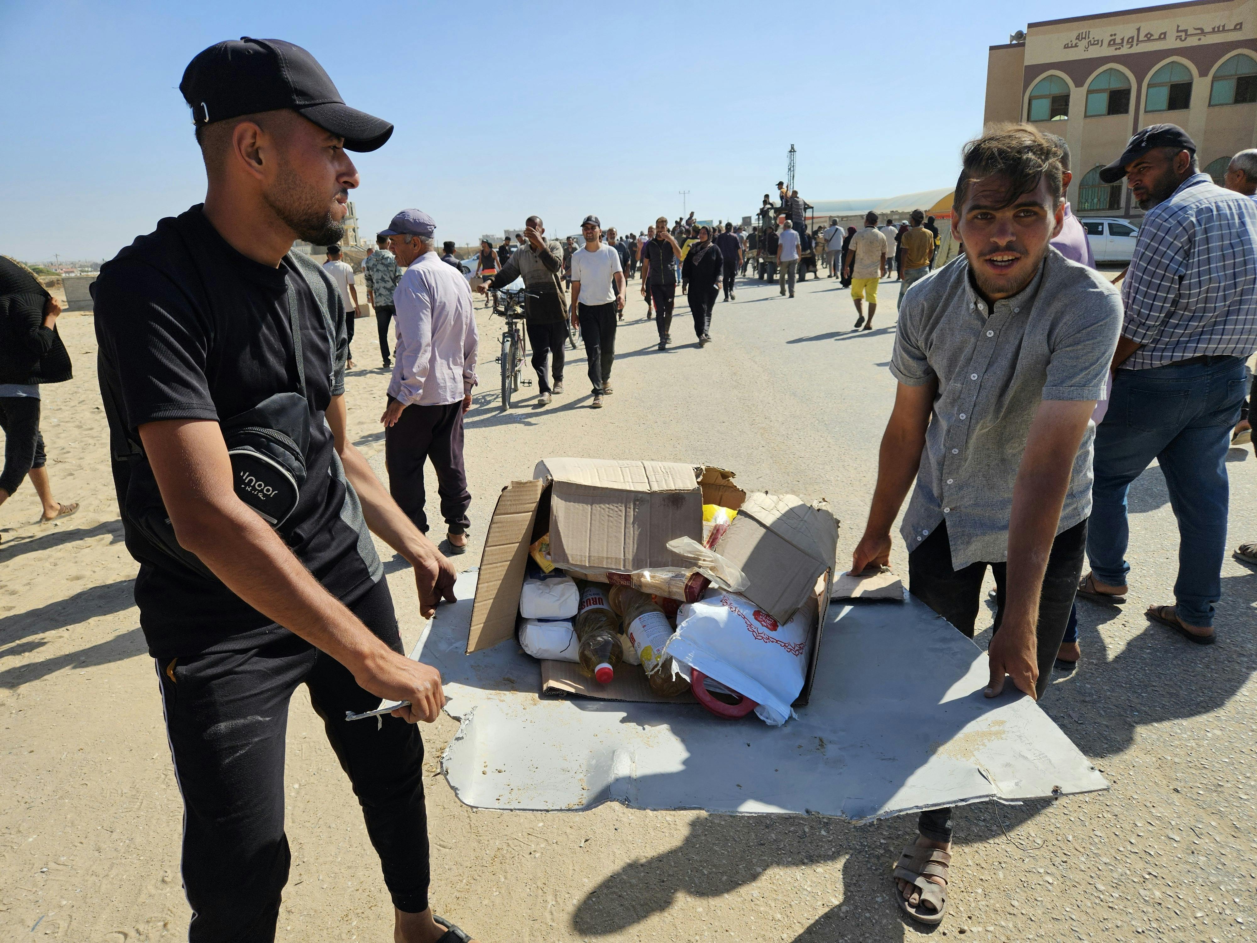Two Palestinians in Gaza hold a box of food containing some flour and cooking supplies. 