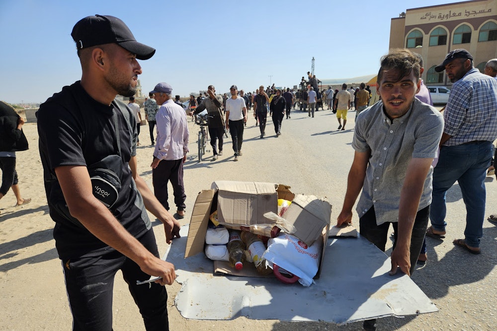 Two Palestinians in Gaza hold a box of food containing some flour and cooking supplies.