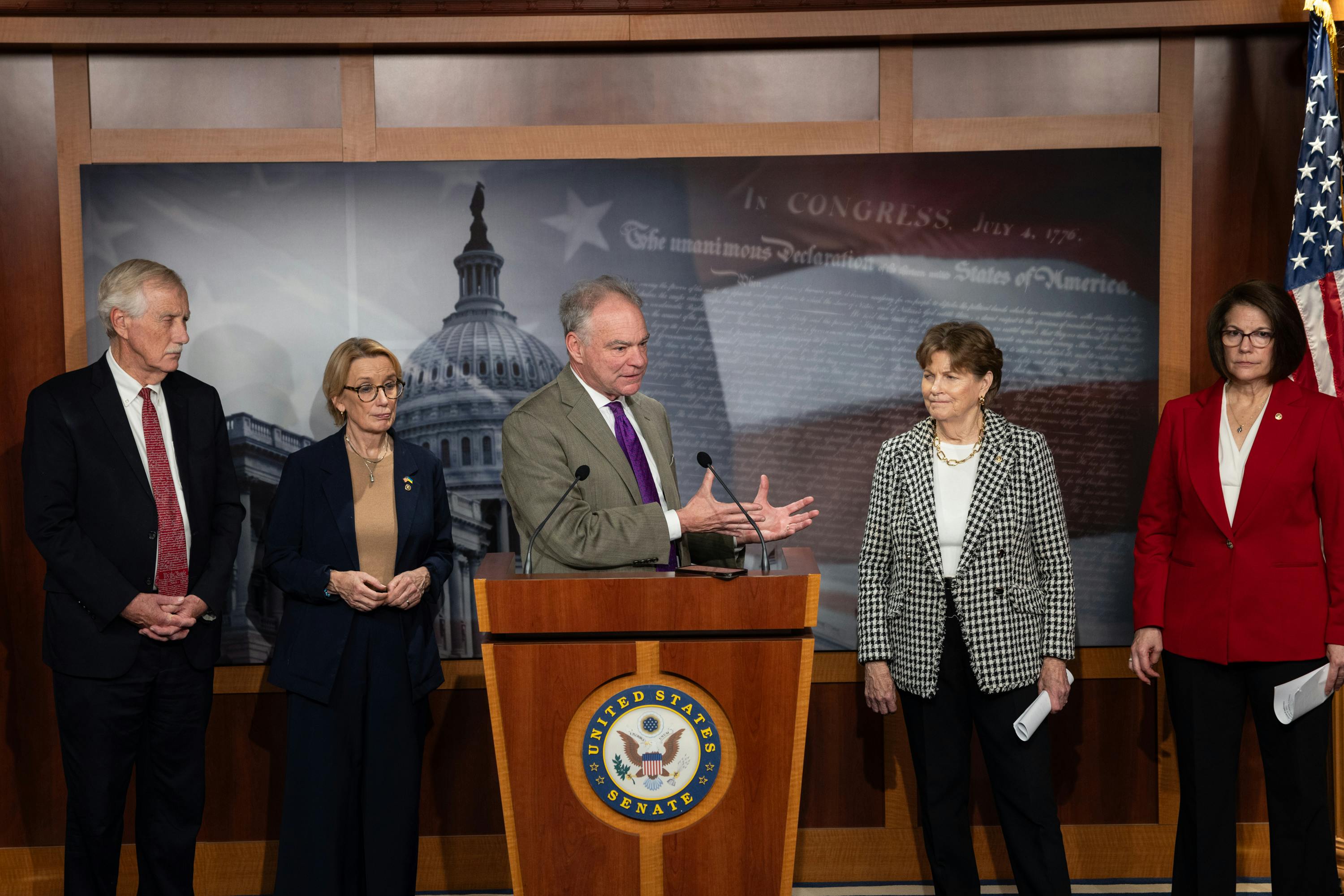 Senator Tim Kaine speaks at a podium about ending the shutdown. He is flanked by Senators Angus King, Maggie Hassan, Jeanne Shaheen, and Catherine Cortez Masto