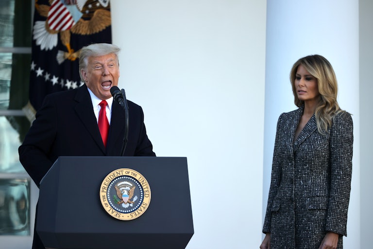 Donald Trump yells at the presidential podium while Melania Trump stands to the side grimacing and looking down