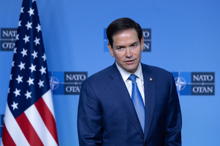 Marco Rubio stands next to a U.S. flag and in front of a NATO backdrop.