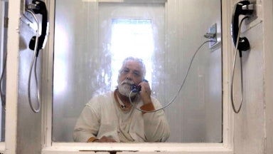 Alvaro Hernandez, better known as Xinachtli, sits behind a layer of glass separating prisoners from visitors in prison.