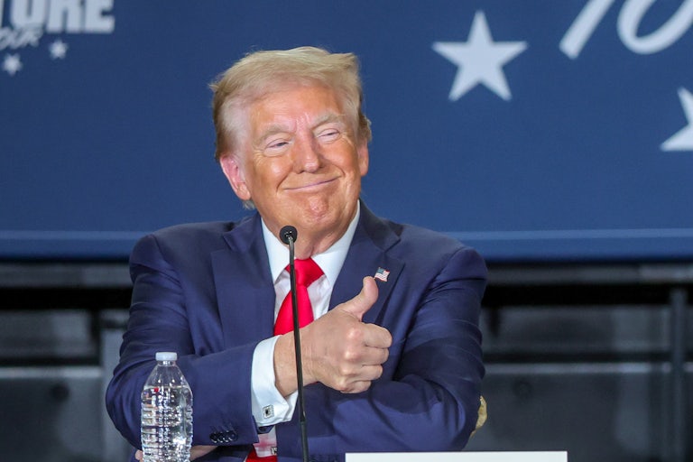 Trump Smiles and gives the thumbs-up sign while seated.