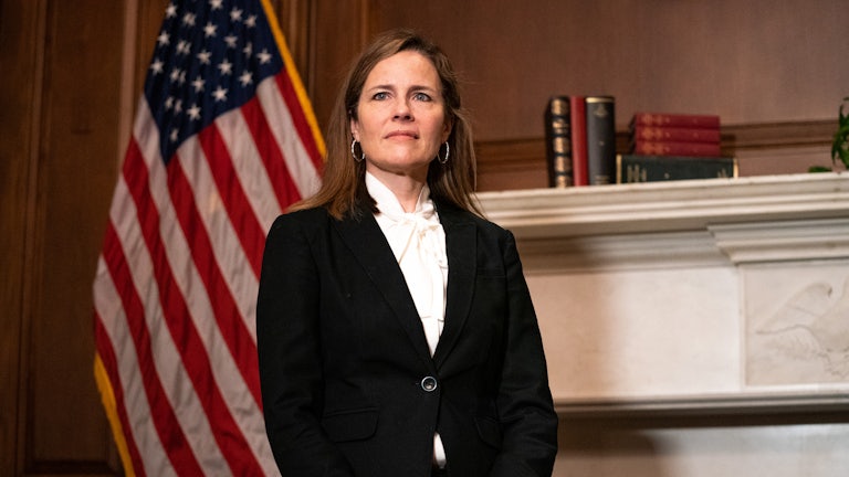 Supreme Court Justice Amy Coney Barrett stands in front of an American flag.