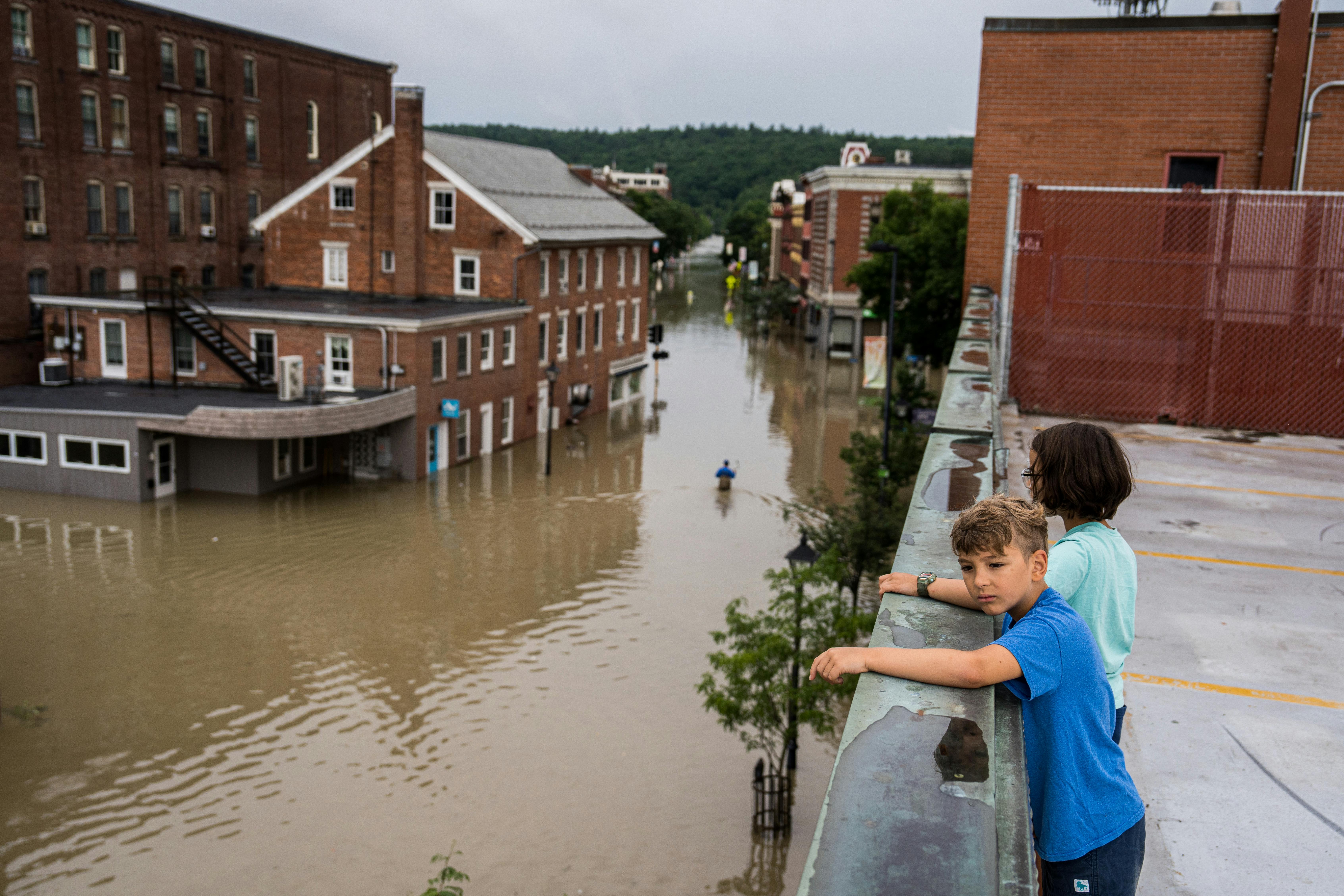 Two children standing on a roof look down at the flooding in Montpeliar, Vermont.