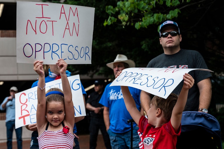 A group of white children and adults hold up signs during a rally against "critical race theory" being taught in schools at the Loudoun County Government center in Leesburg, Virginia