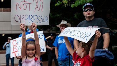 A group of white children and adults hold up signs during a rally against "critical race theory" being taught in schools at the Loudoun County Government center in Leesburg, Virginia